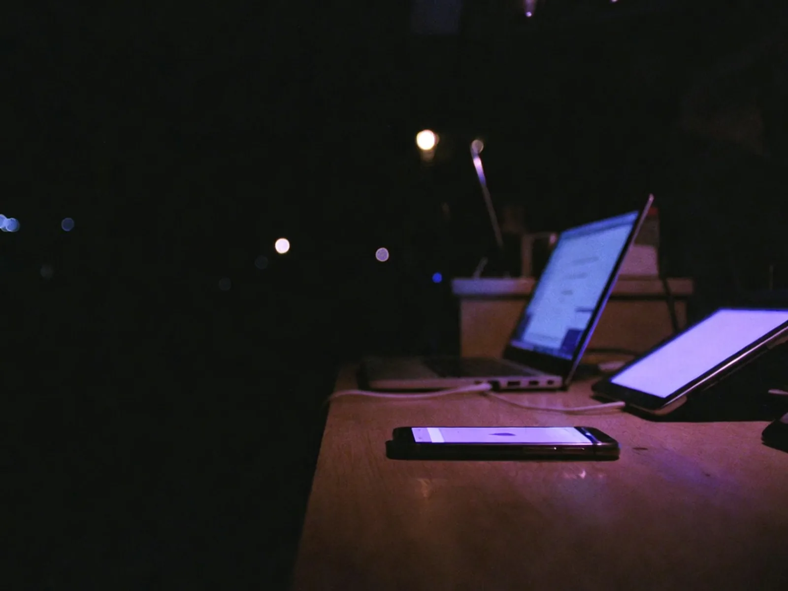 Theke nach Feierabend: ein Handy, ein Laptop und ein Tablet leuchten im selben violetten Licht